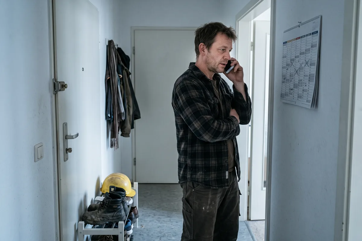 Vermieter telefoniert im Flur einer Monteurwohnung und schaut auf einen Wandkalender